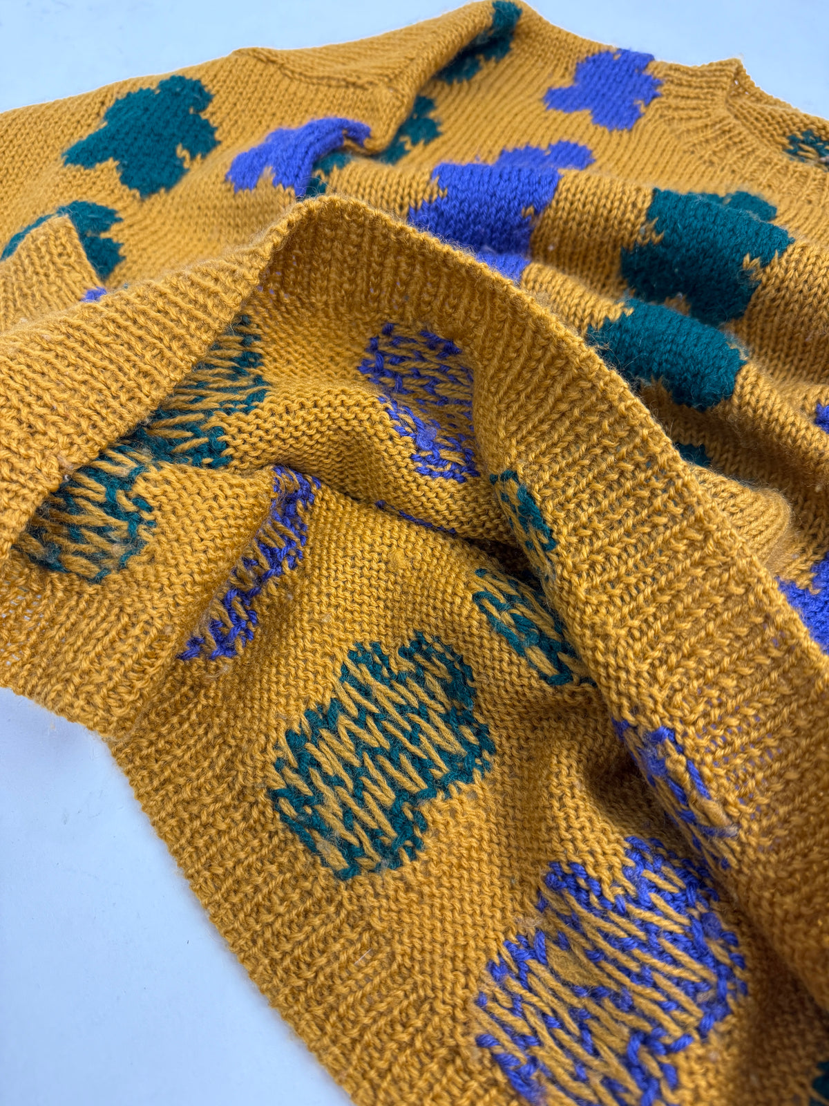 Dettaglio macro maglione jacquard intarsia fatto a mano - trama ocra con motivo verde petrolio e viola, rovescio del lavoro visibile