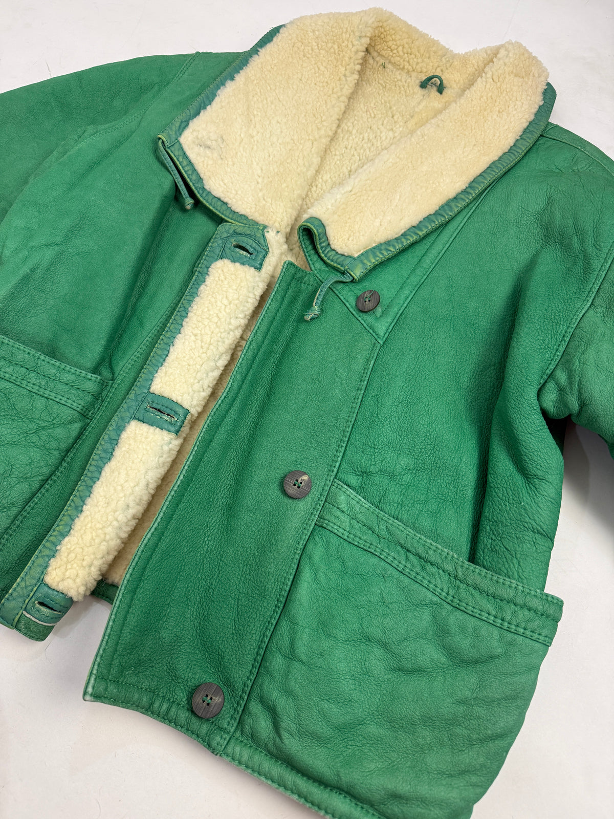 Dettaglio macro colletto e chiusura - colletto revers larghissimo shearling riccio avorio crema, bottone metallo grigio antracite texturizzato, passante pelle verde, pelle agnello verde kelly grana pebbled