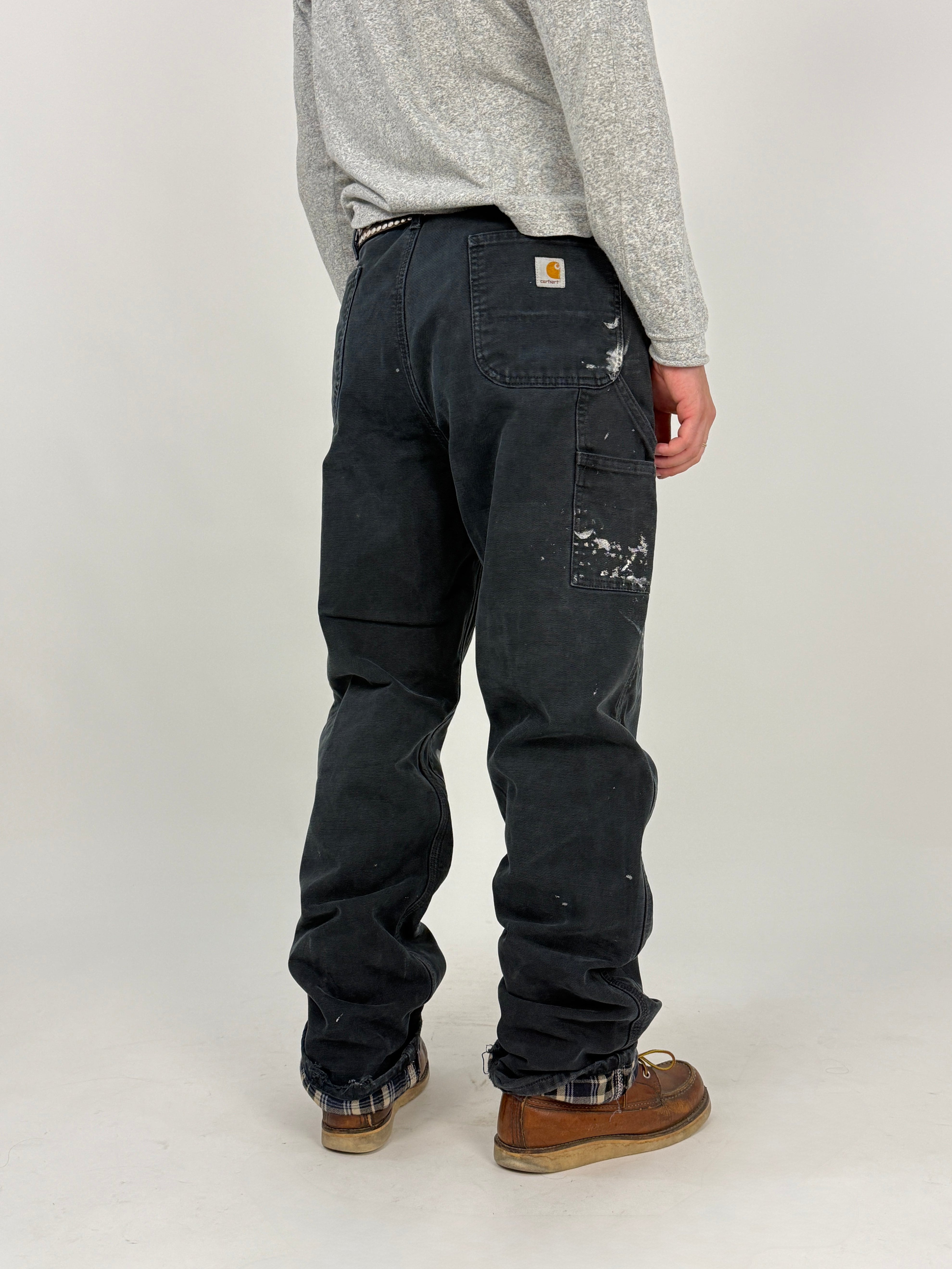 Carhartt Double Knee Flannel-Lined Vintage Nero - vista posteriore con patch Carhartt dorata, tascone cargo e paint splatter bianco/grigio sul retro