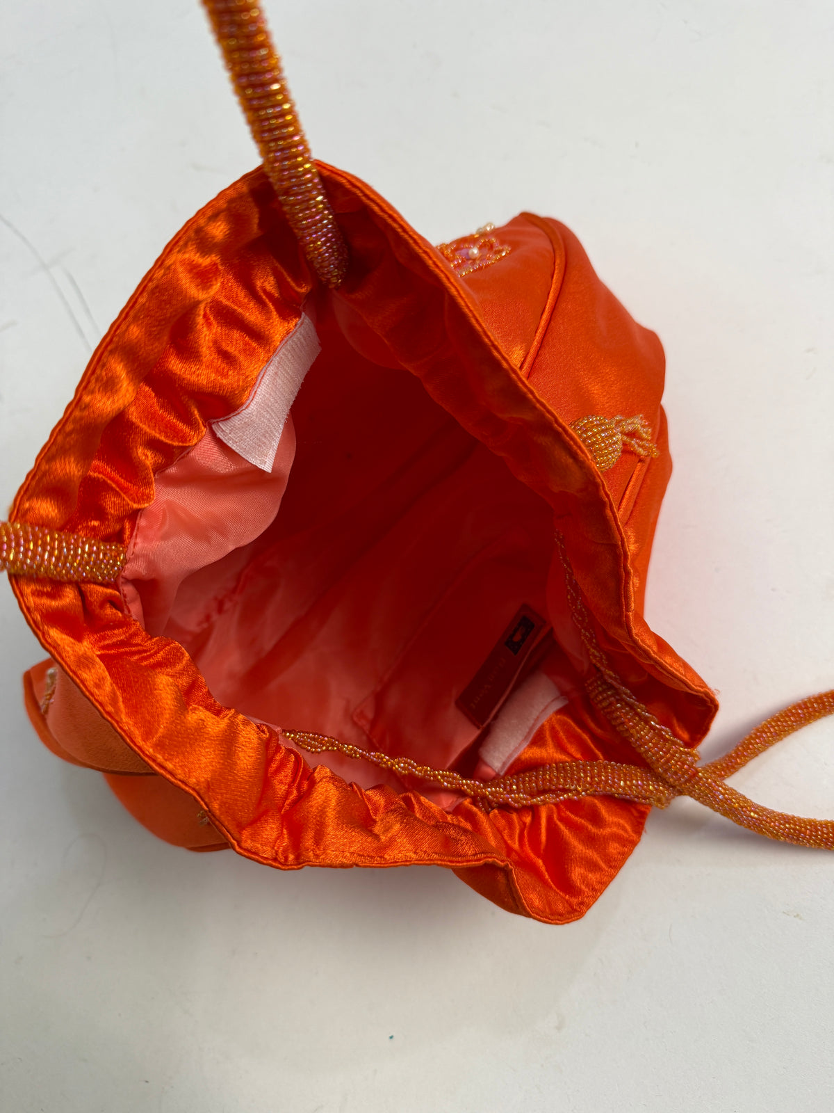 Dettaglio interno borsa - fodera raso arancione, etichetta brand Positano rossa con logo dorato, tasca interna a velcro bianco