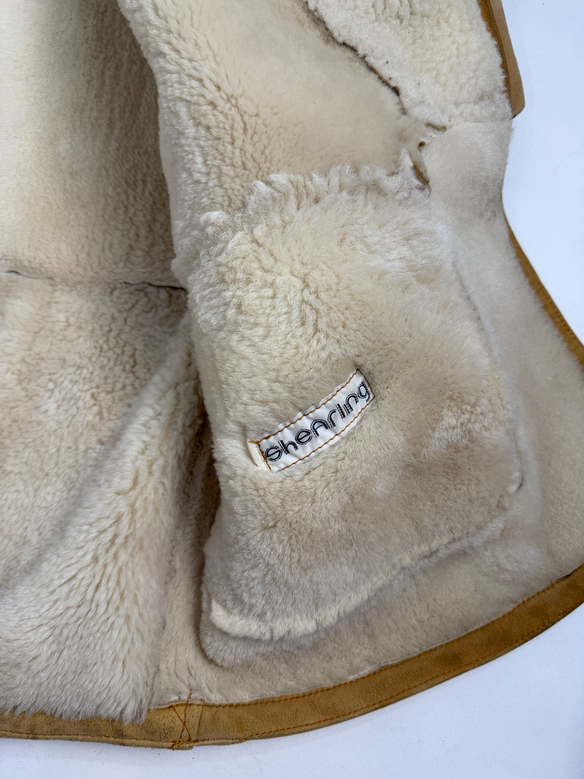 Dettaglio piano colletto aperto - apertura a V profonda colletto shawl shearling avorio, bottone resina avorio petto, pannellatura suede camel con cuciture a vista, polsino risvolto shearling