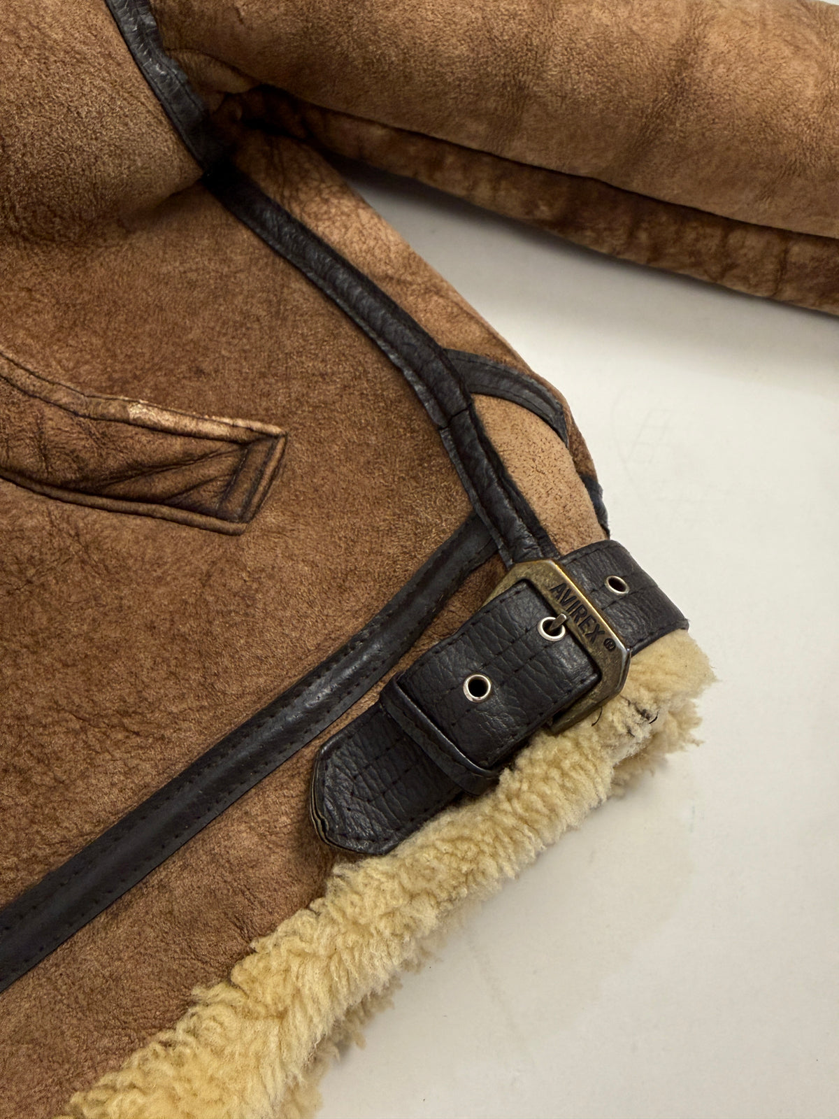 Dettaglio macro fibbia laterale AVIREX orlo - fibbia singola ottone anticato incisione AVIREX con occhielli metallo su cinturino pelle nera, bordo pelle nera goffrata su suede tabacco