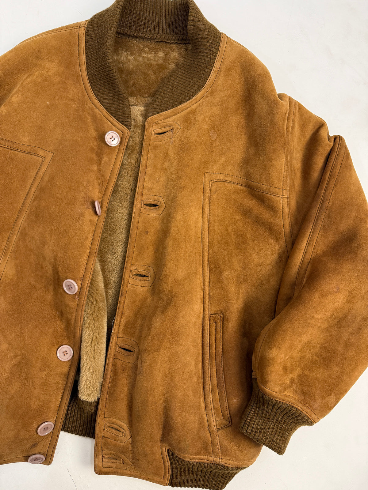 Piano bomber piegato - macro collo costina oliva alta, fodera teddy caramello visibile bordo collo, bottone resina avorio primo piano, cucitura orizzontale petto, polsino costina oliva largo, suede tabacco cuciture vista
