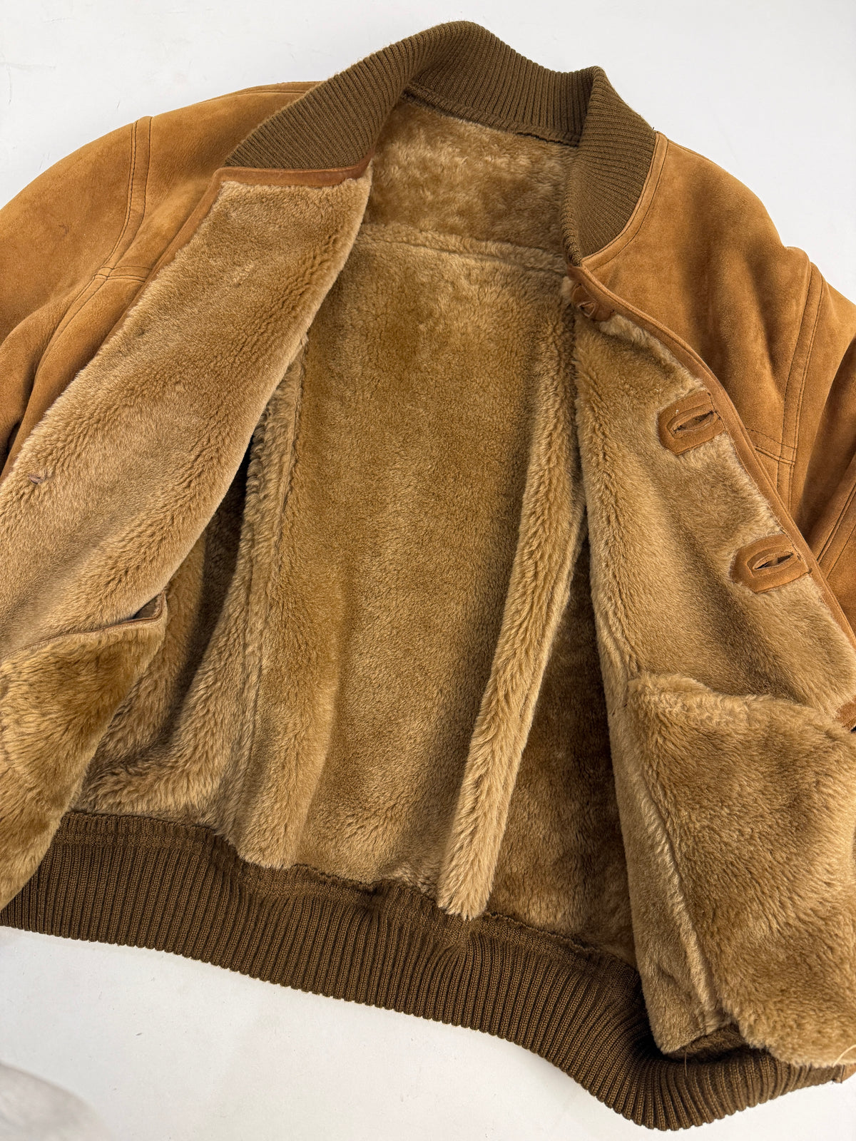 Piano fronte aperta - suede montone tabacco cuoio ambrato, 4 bottoni resina bianco-avorio 4 fori asole orizzontali, tasca toppa grande petto sinistra, tasche basse taglio orizzontale, piccola tasca passamano welt, costine oliva