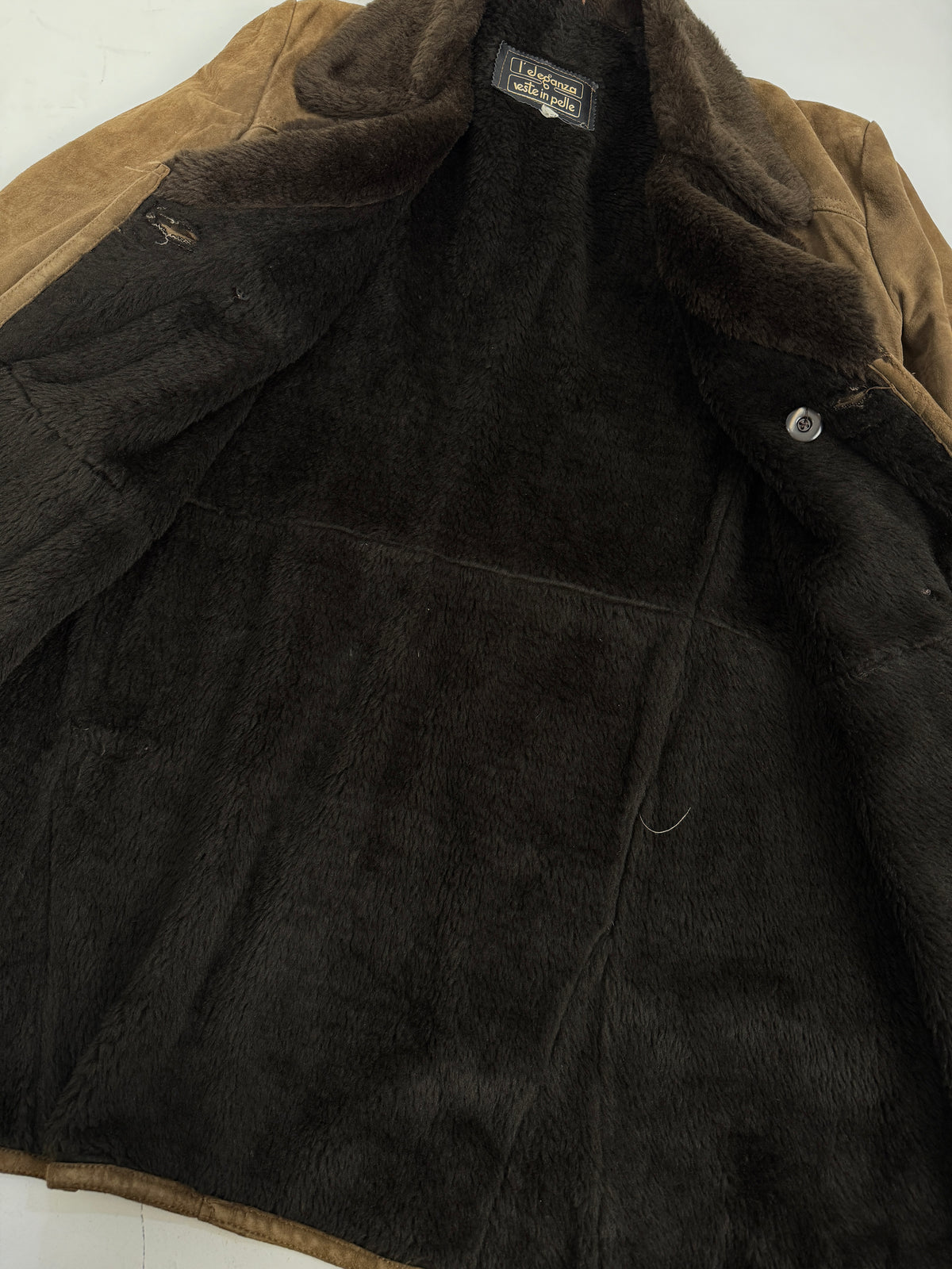 L'Eleganza cappotto suede - macro dettaglio colletto revers shearling rasato marrone cioccolato, etichetta nera L'Eleganza veste in pelle corsivo oro, bottoni circolari neri doppio petto, suede kaki oliva