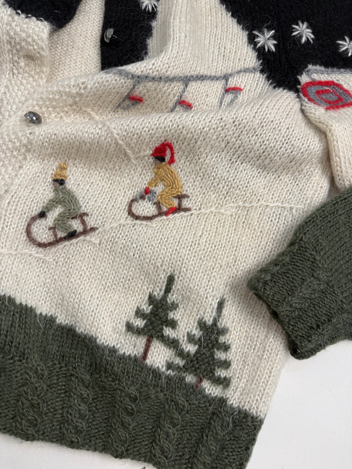Ricami di slittini e abeti sul cardigan panna