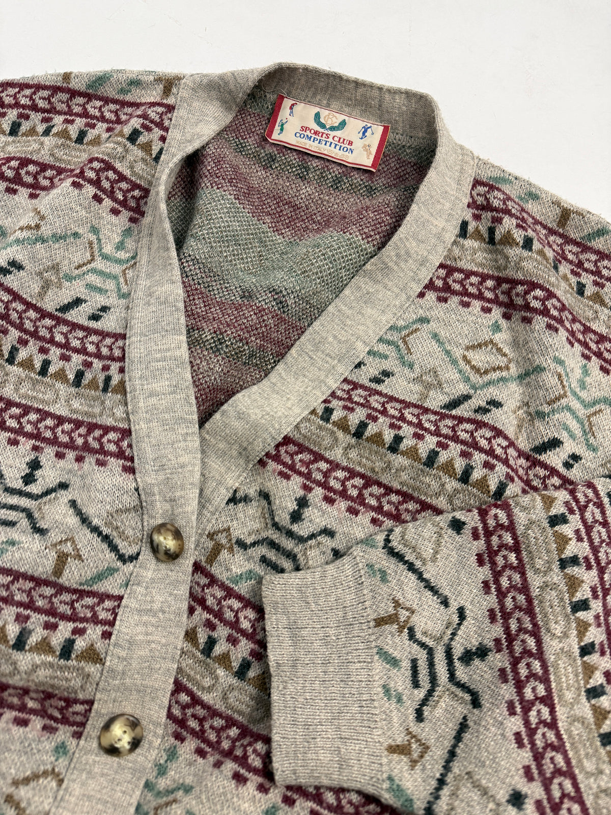 Dettaglio collo e etichetta cardigan Sports Club Competition - etichetta illustrata con golfisti, collo V con bordura costina grigia, bottone dorato inciso, punto jacquard misto lana